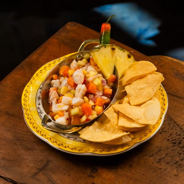 Ceviche with shrimp, pineapple, and chips on a yellow plate, garnished with a chili.
