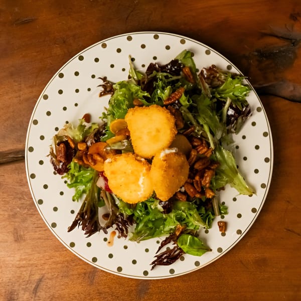 Starlite Restaurant's fresh green salad with fried goat cheese, pecans, and mushrooms on a polka-dotted plate.