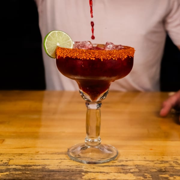 A bartender pours red liquid into a Starlite margarita with a chili-lime rim and lime wedge.