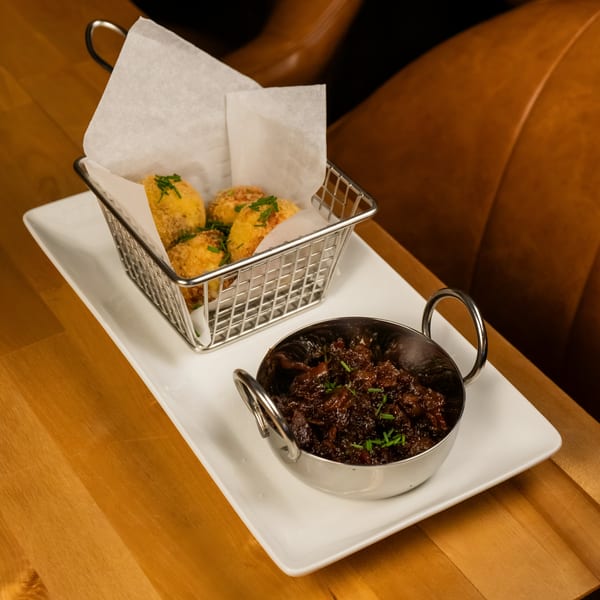Starlite Restaurant's fried appetizers in a metal basket and a small bowl of dark sauce with chives.