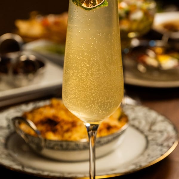 Bubbly cocktail with a lime garnish, served with a side of baked mac and cheese.