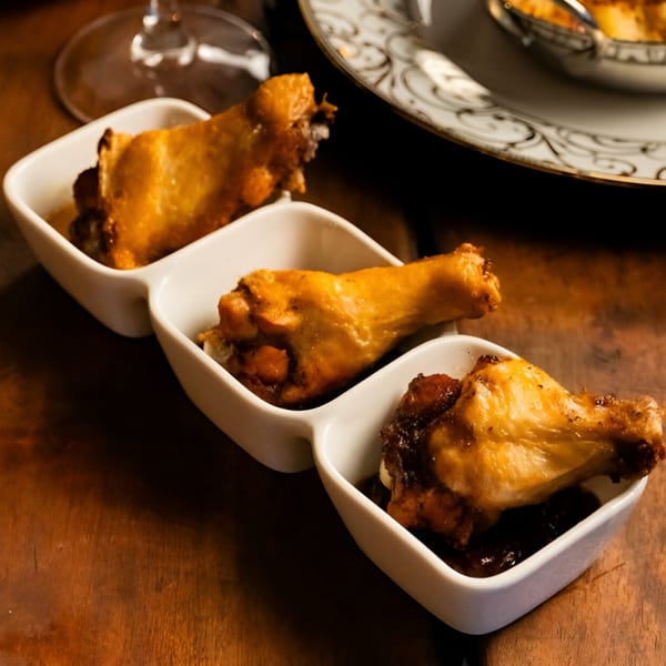 Three golden-brown chicken drumettes in white rectangular dishes on a wooden table at Starlite Restaurant.